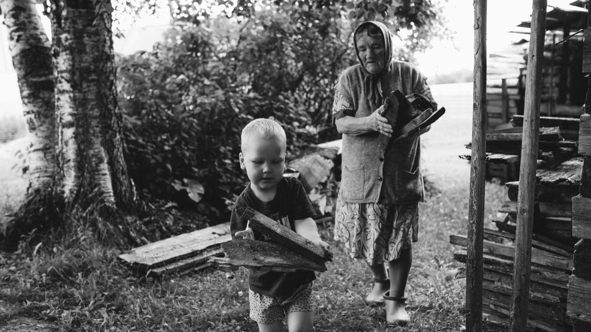 A touching black and white scene of a grandmother with her grandson gathering firewood outdoors.