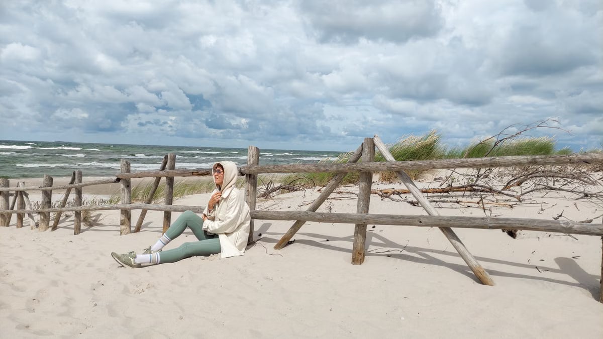 Person in casual attire sits on Baltic beach, enjoying the serene sea view.